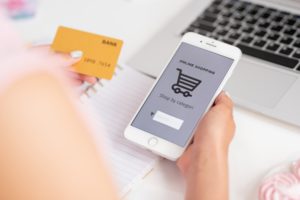 Young consumer of online shop with smartphone and banking card searching goods