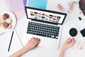 top view of woman drinking coffee with macaroon while using laptop with pinterest website