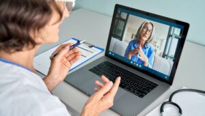 Female doctor consulting older senior patient during virtual video call visit.