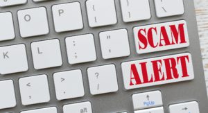 White computer Keyboard with red keys that says SCAM ALERT, online dangers Concept
